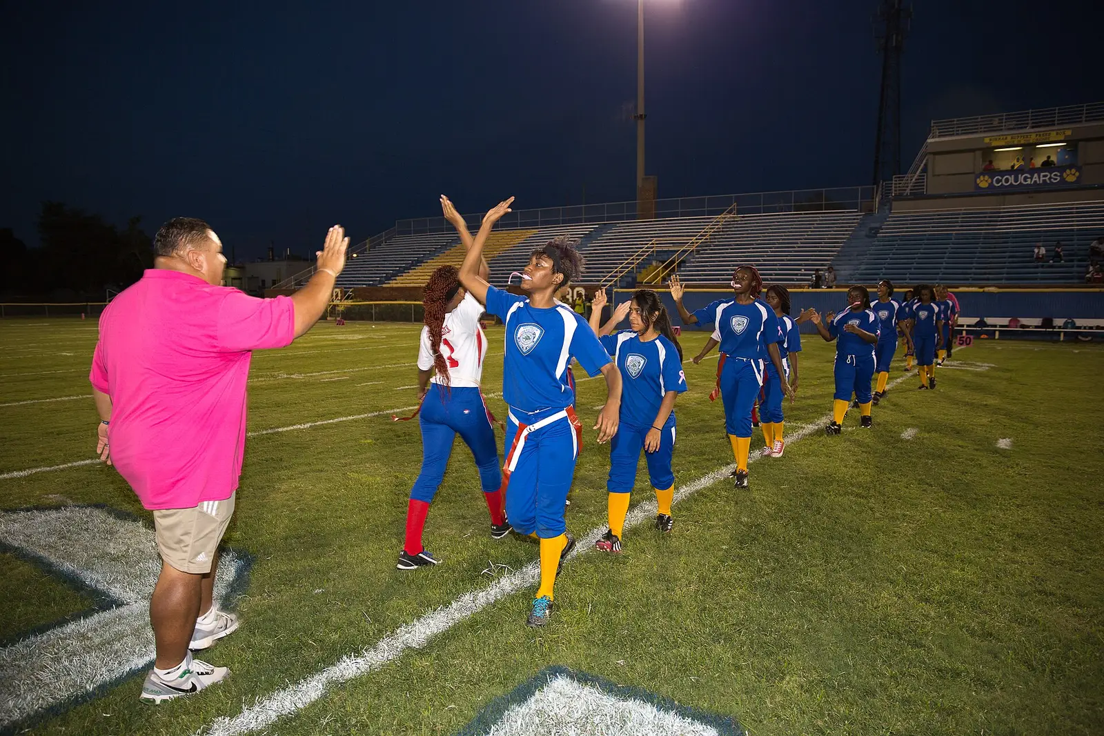 Players and a coach slap hands under the stadium lights at a North Charleston police league football game.