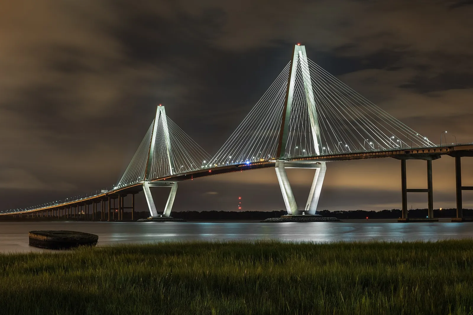 The Arthur Ravenel Jr. Bridge lit up at night over the Cooper River, seen from the Mount Pleasant shore.